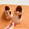 Hand holding a pair of beige baby T-strap shoes