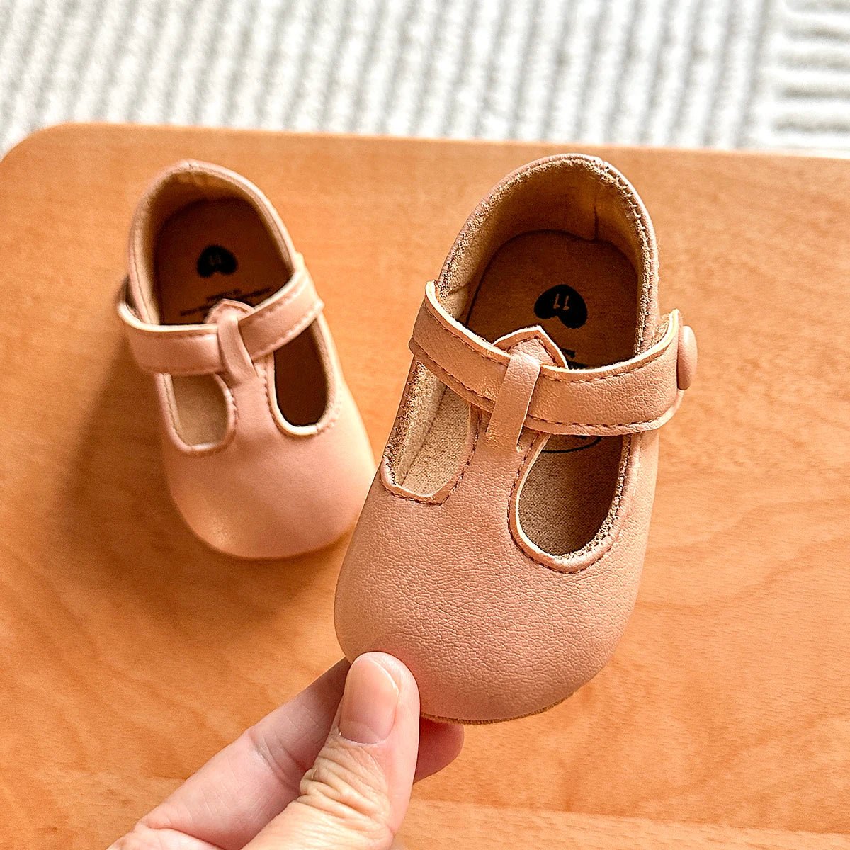 Hand holding a pair of beige baby T-strap shoes