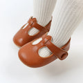 Baby foot in a white sock wearing a brown T-strap shoe