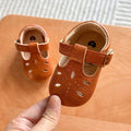 Hand holding a pair of light brown baby T-strap shoes