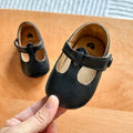 Hand holding a pair of black baby T-strap shoes