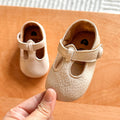 Hand holding a pair of cream baby T-strap shoes with perforated sides