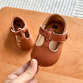 Hand holding a pair of brown baby T-strap shoes