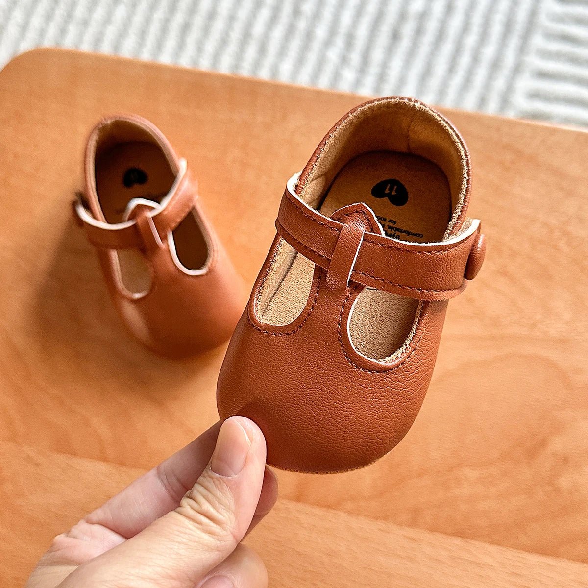 Hand holding a pair of brown baby T-strap shoes
