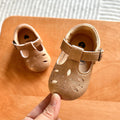 Hand holding a pair of camel baby T-strap shoes