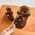 Hand holding a pair of dark brown baby T-strap shoes