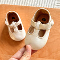 Hand holding a pair of white baby T-strap shoes