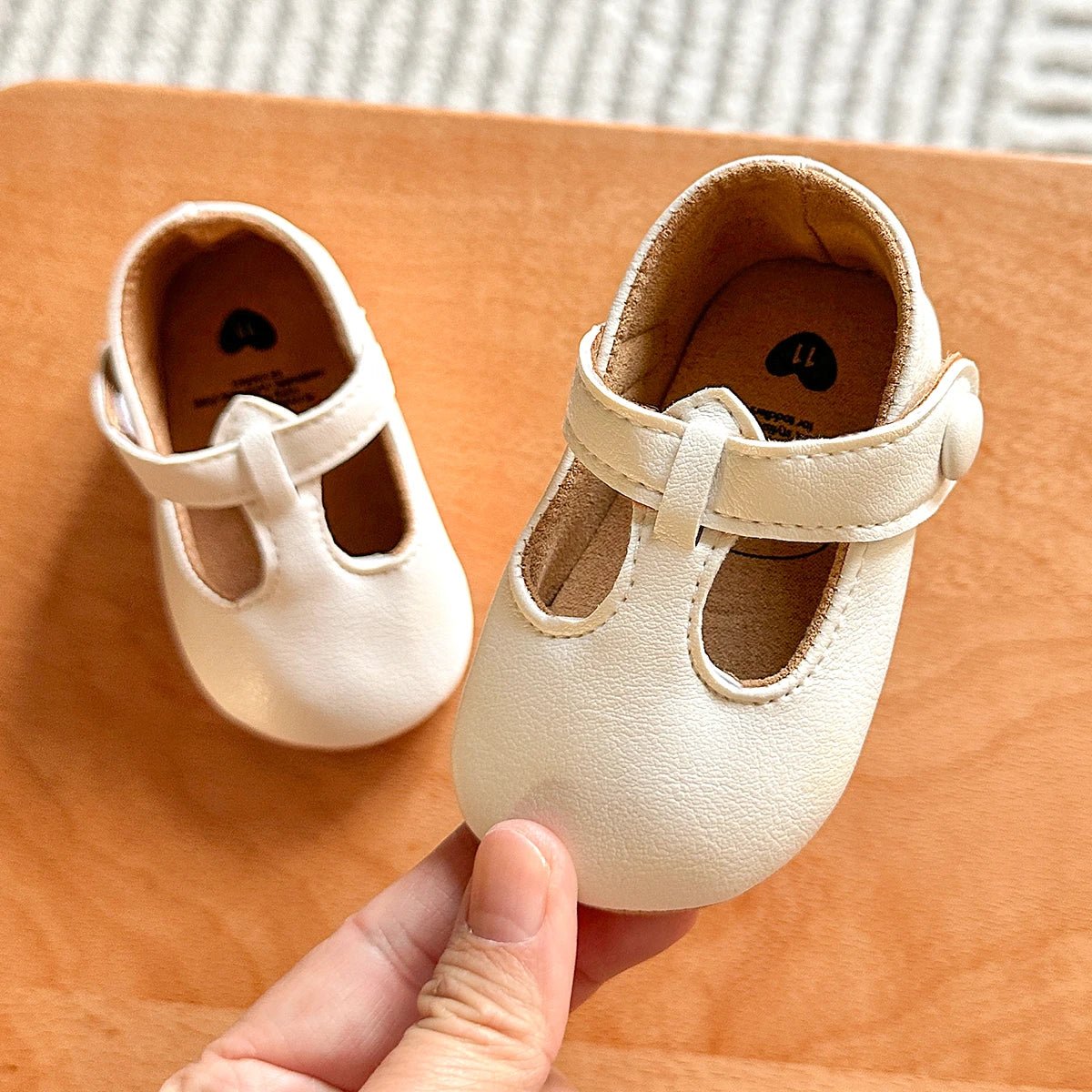 Hand holding a pair of white baby T-strap shoes