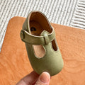 Hand holding a pair of army green baby T-strap shoes