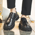 Black lace-up brogue-style shoes with thick black lug soles, worn with black trousers