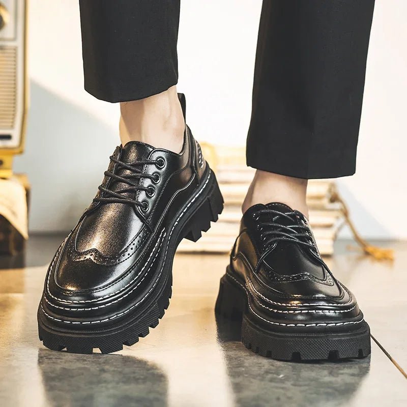 Black lace-up brogue-style shoes with thick black lug soles, worn with black trousers