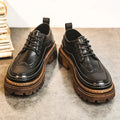 Pair of black lace-up brogue-style shoes with thick brown lug soles on a grey carpet
