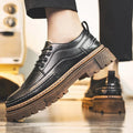 Black lace-up brogue-style shoe with a thick brown lug sole worn from the side with black trousers