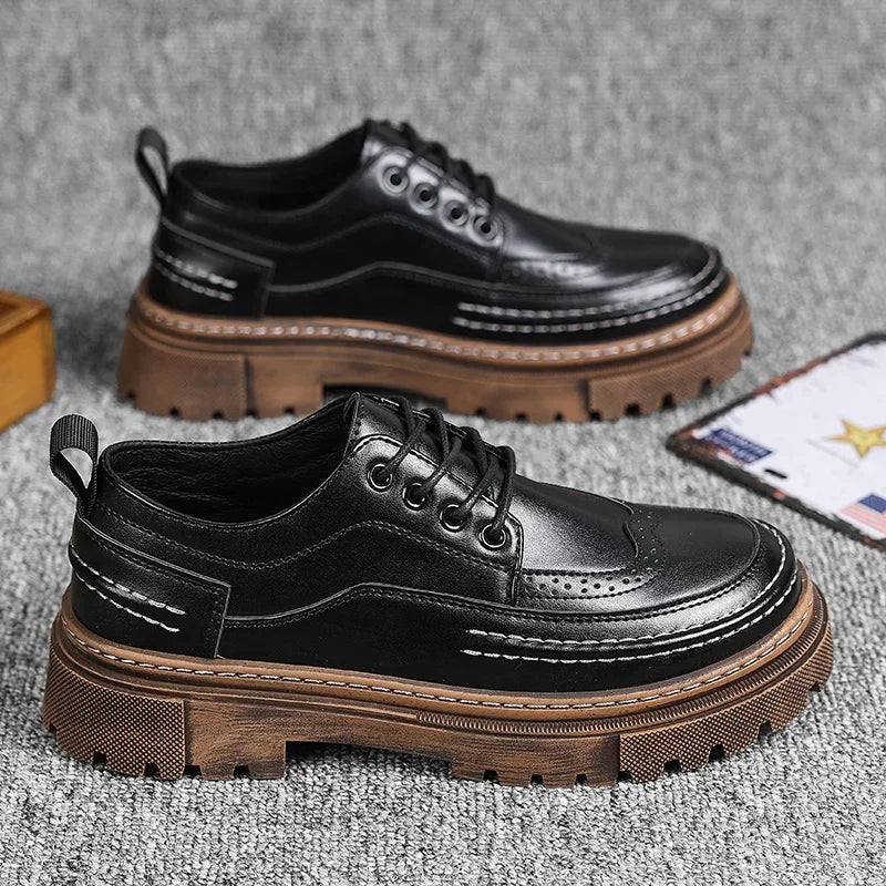 Pair of black brogue-style shoes with brown lug soles on a grey surface, with a card beside them