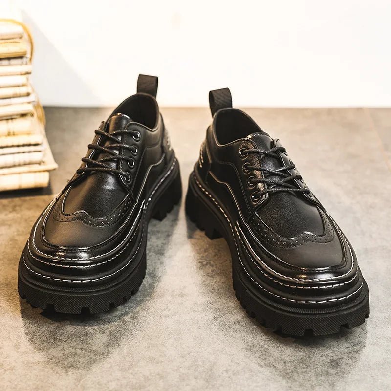 Pair of black lace-up brogue-style shoes with thick black lug soles on a grey carpet