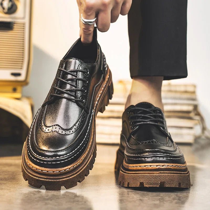 Black lace-up brogue-style shoes with a thick brown lug sole, worn with black trousers and tied by hand