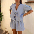 Woman in a blue checked tie-front puff-sleeve top and matching shorts in a bright room