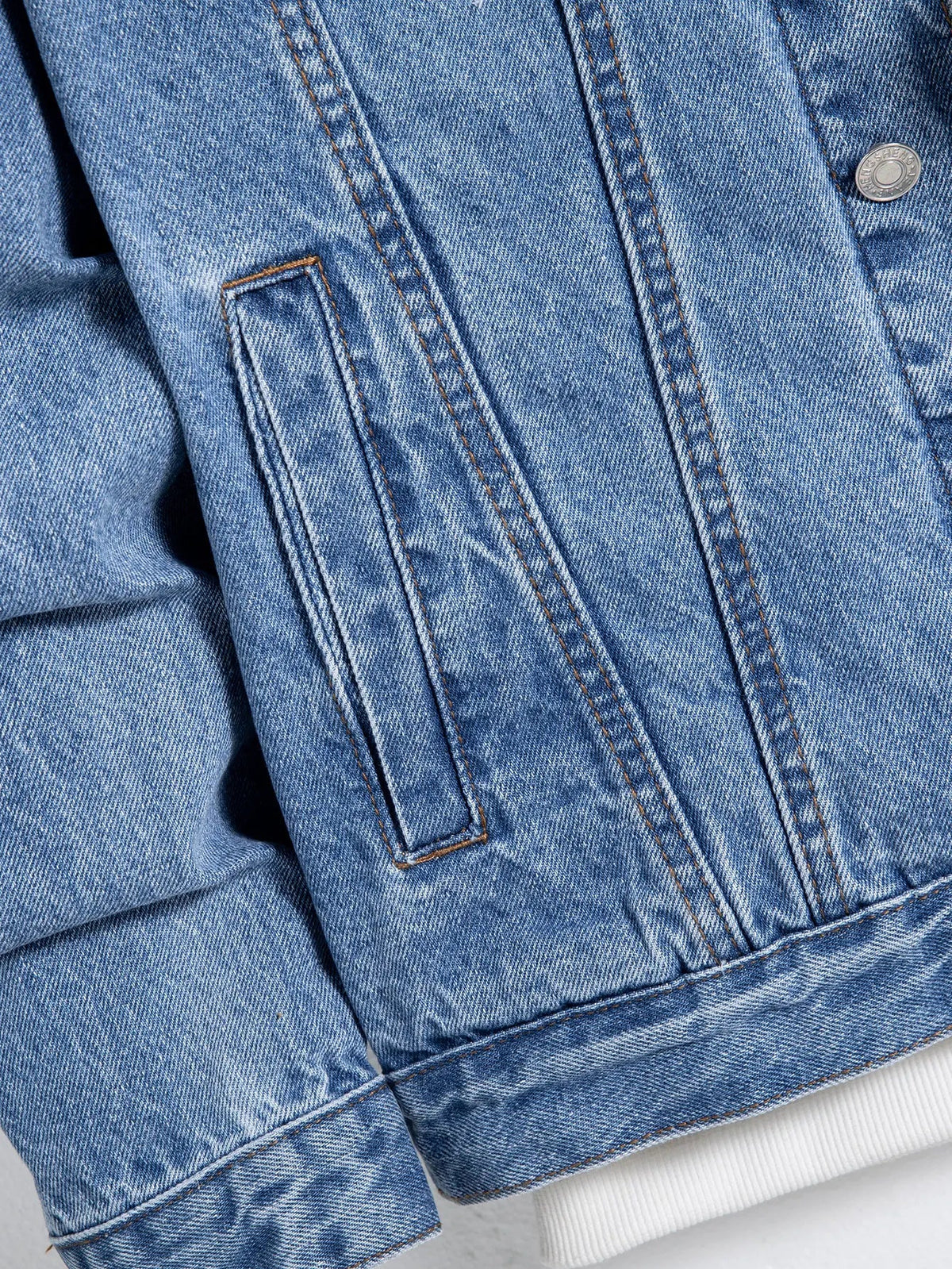 Close-up of a denim jacket side pocket, buttoned cuff and hem
