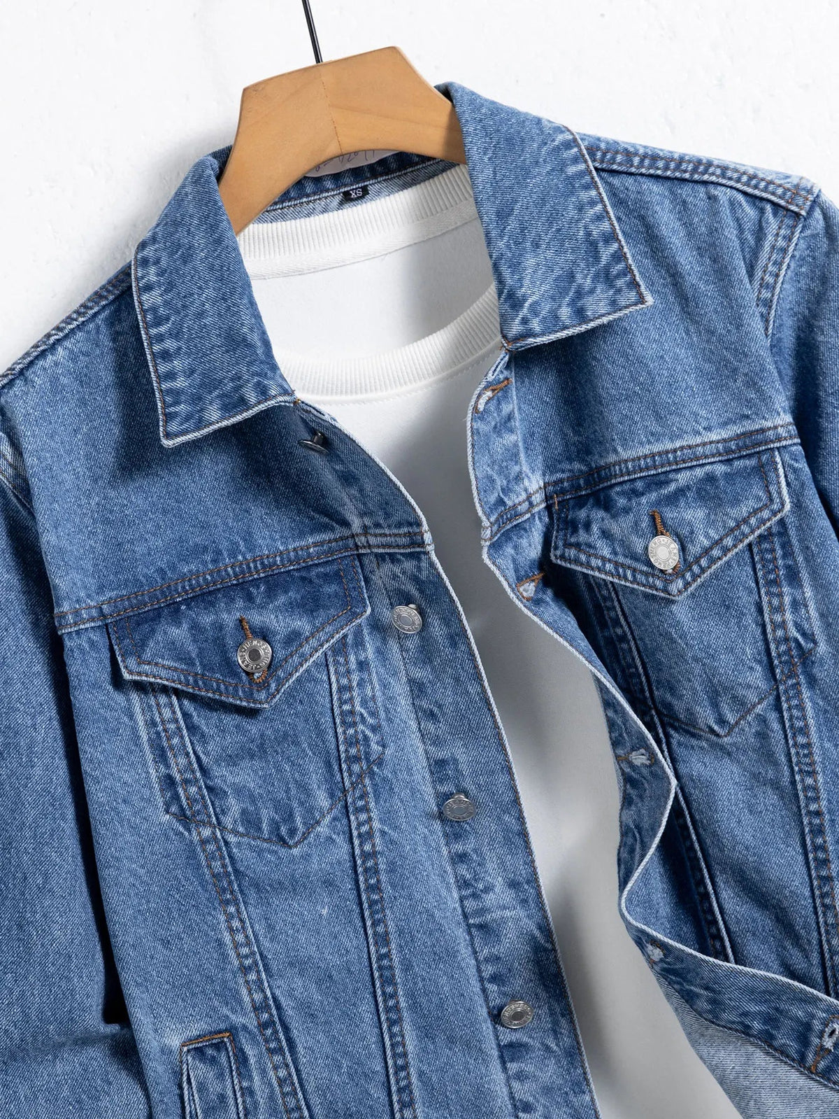 Close-up of a blue denim jacket collar and chest flap pocket over a white t-shirt