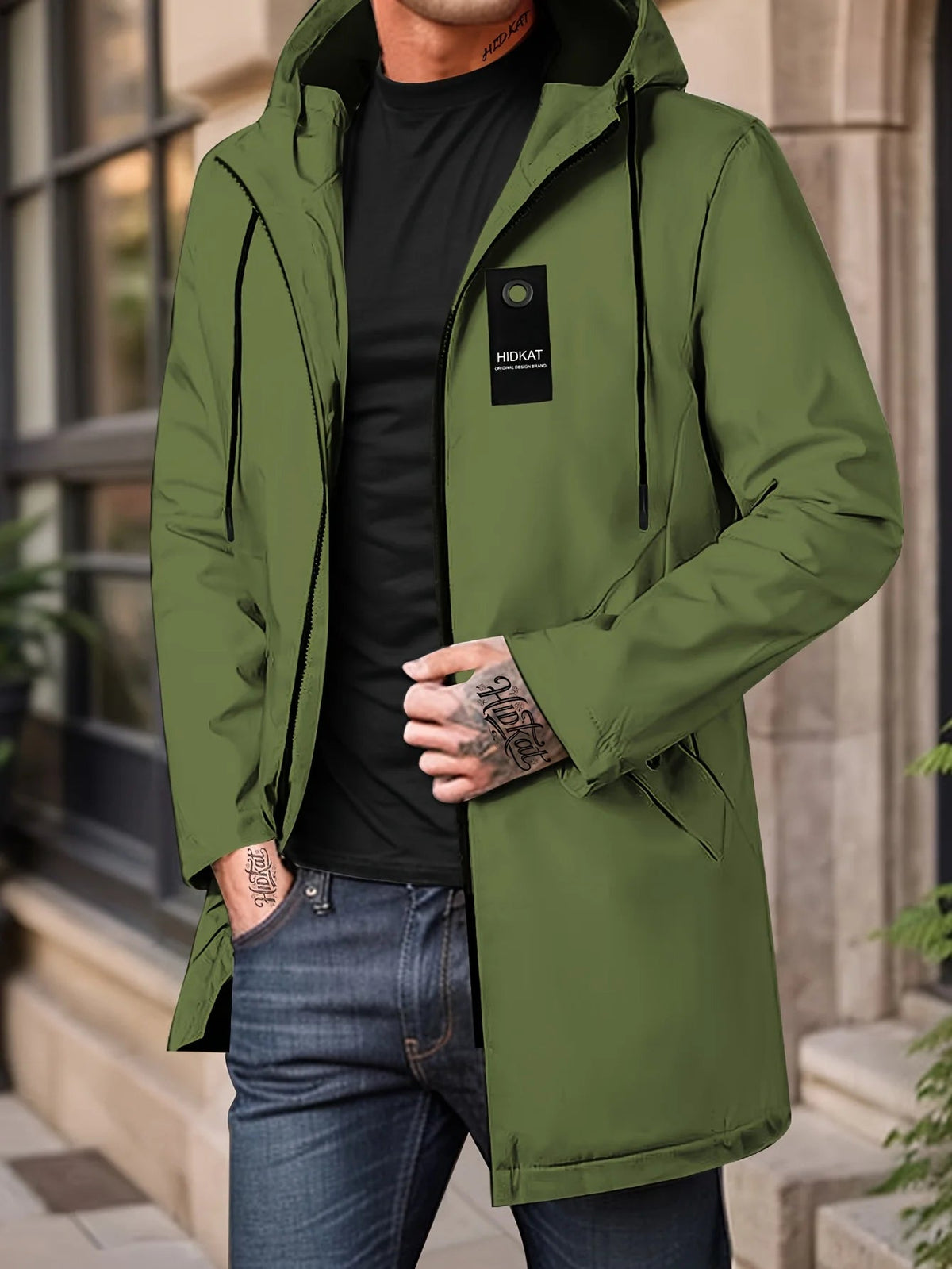 Man in a green mid-length hooded zip jacket with a small tag, standing on a city street