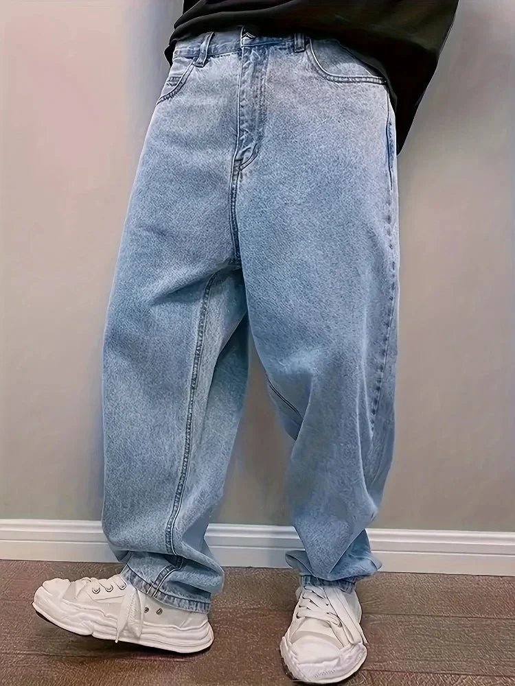 Man in light blue washed baggy jeans and white sneakers standing against a wall, front view