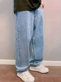 Side view of light blue baggy wide-leg jeans worn with white sneakers on a wooden floor