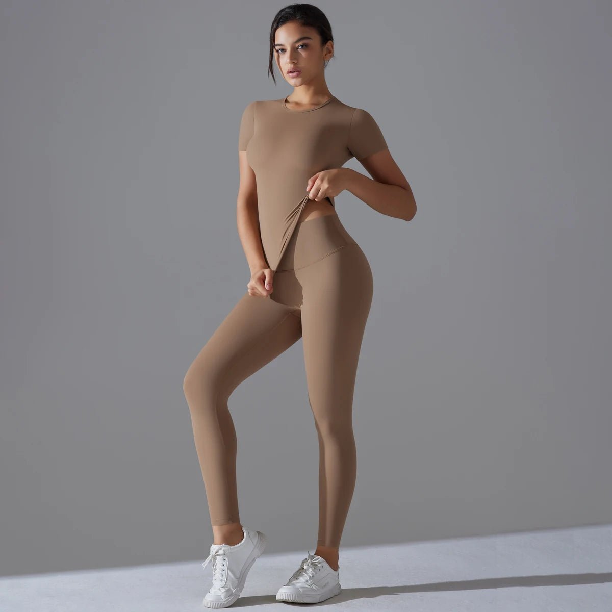 Woman in a tan-brown short-sleeve top and matching leggings with one hand at the waist