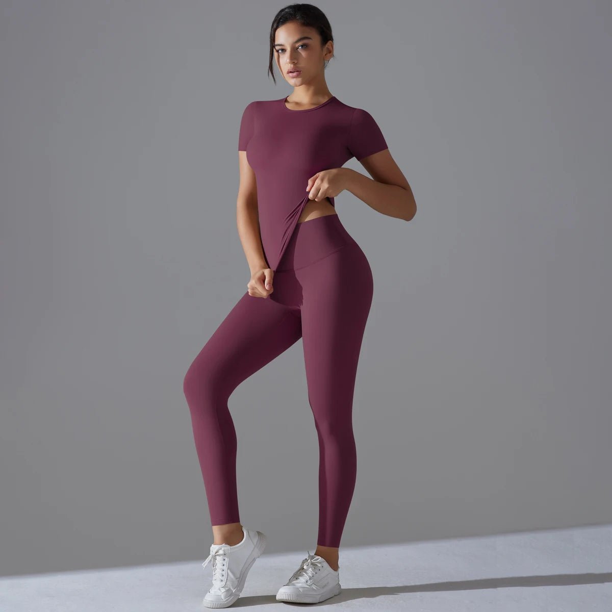 Woman in a burgundy short-sleeve top and matching leggings with one hand at the waist