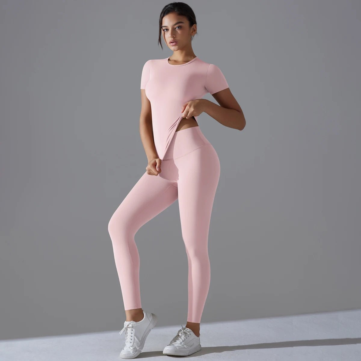 Woman in a light pink short-sleeve top and matching leggings with one hand at the waist