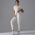 Woman in a cream white short-sleeve top and matching leggings with one hand at the waist