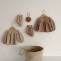 Gingham baby tops and bloomers hanging beside a woven basket