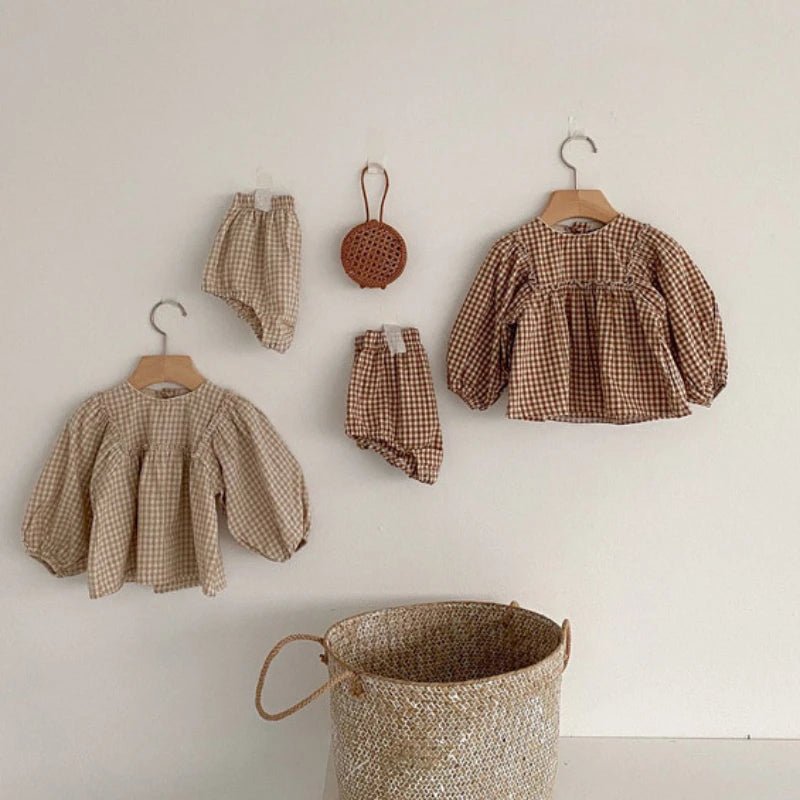 Gingham baby tops and bloomers hanging beside a woven basket
