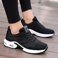 Black knit lace-up sneakers with a thick white air-cushion sole, worn by a woman tying her laces