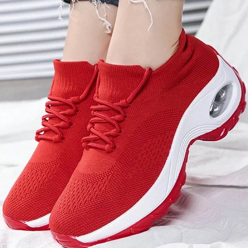 Red knit slip-on sneakers with laces and a thick white air-cushion sole, worn with an ankle chain