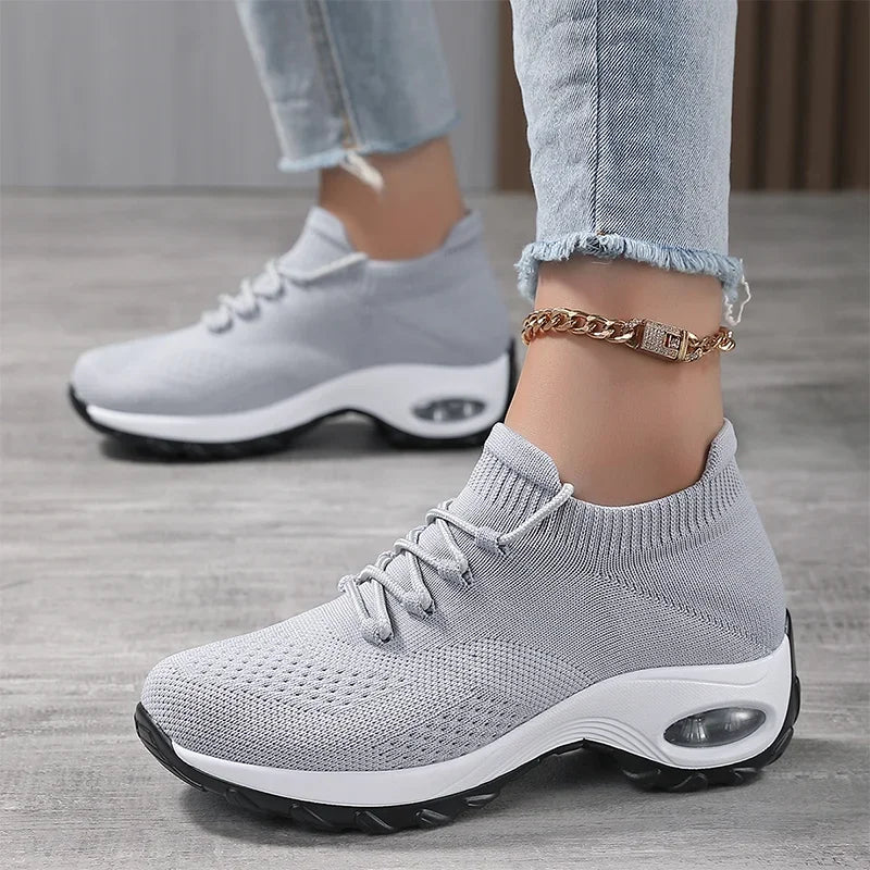 Grey knit slip-on sneakers with laces and a thick white air-cushion sole, worn with cropped jeans