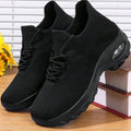 Pure black knit slip-on sneakers with laces and a chunky air-cushion sole on a bookshelf