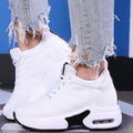 White high-top style lace-up sneakers with a visible air-sole heel, worn with ripped jeans