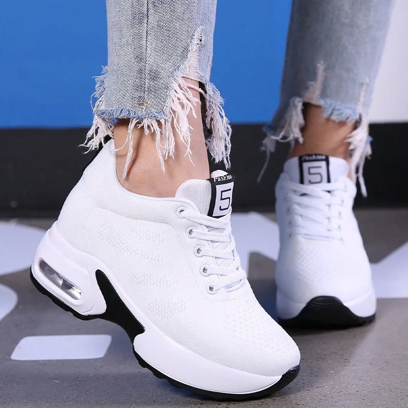 White lace-up sneakers with a raised cushioned sole worn with ripped jeans, three-quarter view
