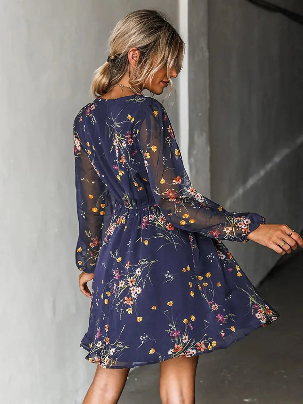 Back and side view of a navy floral mini dress with sheer long sleeves worn with hair up