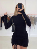 Woman in a black long-sleeve ruched mini dress with a side drawstring and high neck